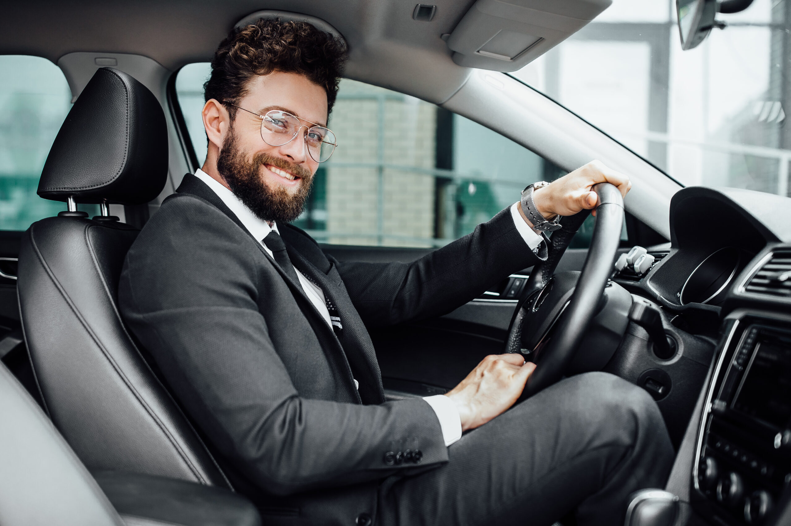 handsome young businessman in full suit smiling while driving a new car.